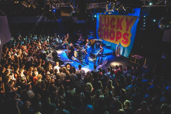 Plný klub pod pódiem s banerem Lucky Chops